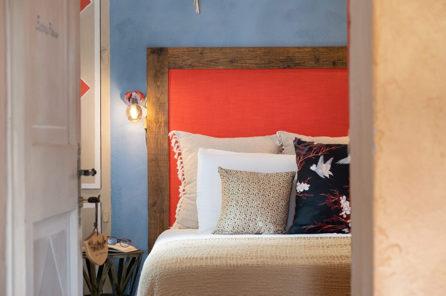 Cozy bedroom featuring a vibrant red headboard, decorative pillows, and warm lighting against a blue wall, with a glimpse of a wooden door and stylish furnishings. Ideal for relaxation and comfort. | Only on SopranoVillas