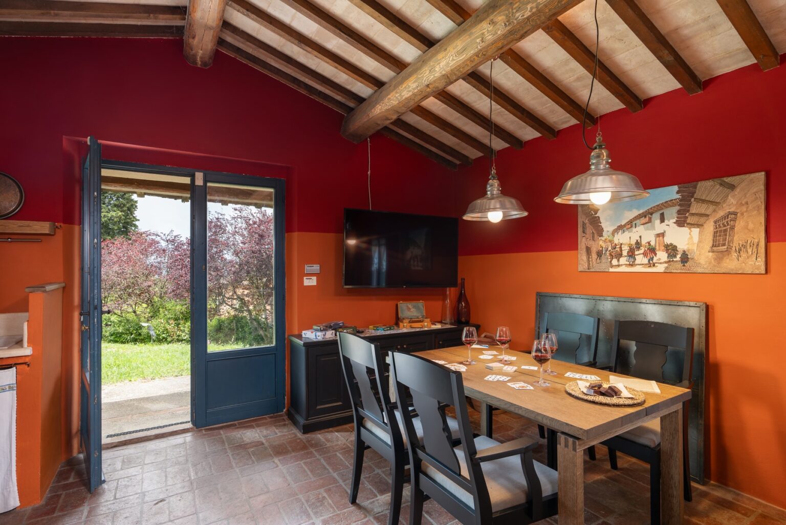Cozy dining area in a rustic cabin featuring wooden beams, a table set for a meal, and large windows opening to a garden view. | Only on SopranoVillas