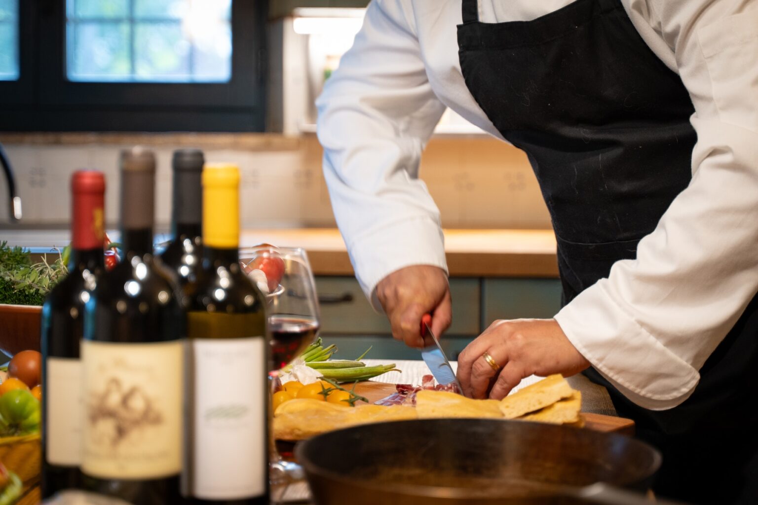 Chef preparing ingredients on a wooden cutting board, with bottles of red wine and a glass nearby, in a well-lit kitchen setting. | Only on SopranoVillas