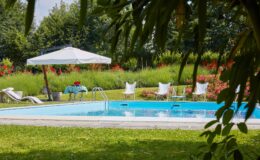 Serene outdoor swimming pool surrounded by lush greenery and vibrant flowers, featuring lounge chairs, a shaded seating area with a table, and a relaxing atmosphere perfect for leisure and relaxation.