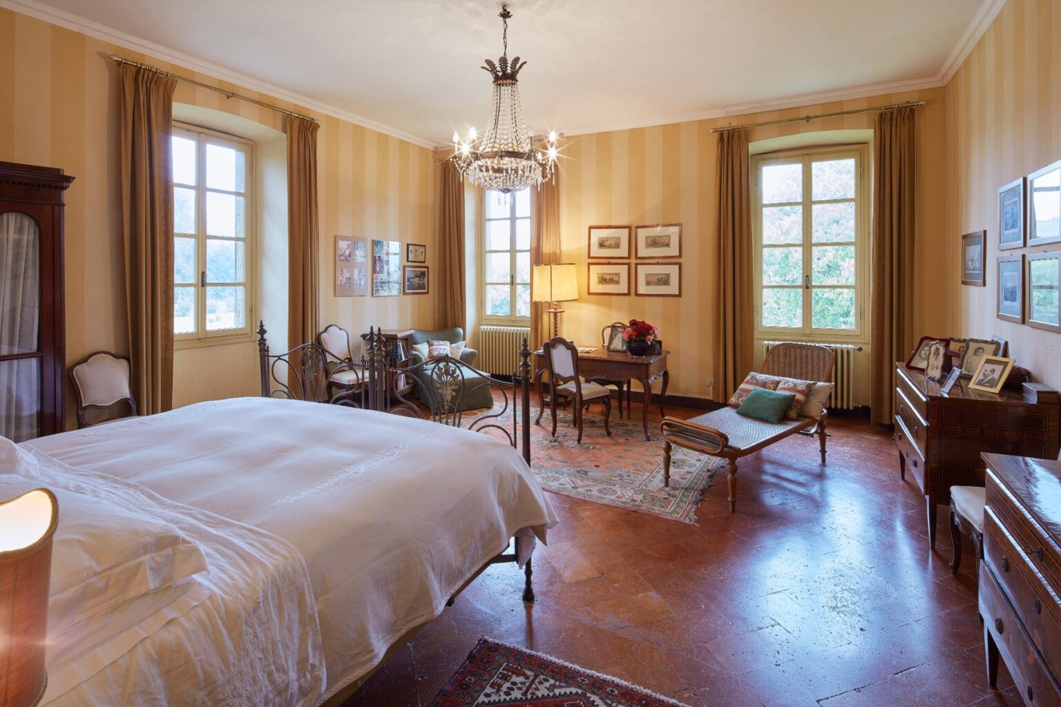 Spacious and elegantly decorated bedroom featuring a large bed, vintage furniture, and ample natural light from tall windows. The room includes a cozy seating area, a writing desk, and decorative artwork on the walls, creating a warm and inviting atmosphere. | Only on SopranoVillas