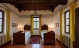 Cozy guest room featuring two wooden twin beds with floral bedding, yellow curtains, and rustic beams. The room is illuminated by a bedside lamp and showcases framed artwork on the walls, offering a warm and inviting atmosphere.