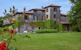 Historic villa surrounded by lush gardens and blooming roses, featuring ivy-covered walls and traditional architecture under a clear blue sky. Ideal for nature lovers and photography enthusiasts.