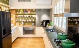 Modern kitchen interior featuring sleek cabinetry, a stylish backsplash with geometric patterns, stainless steel appliances including a refrigerator and oven, and green cookware on the stove. Natural light streams in through large windows, enhancing the inviting atmosphere.