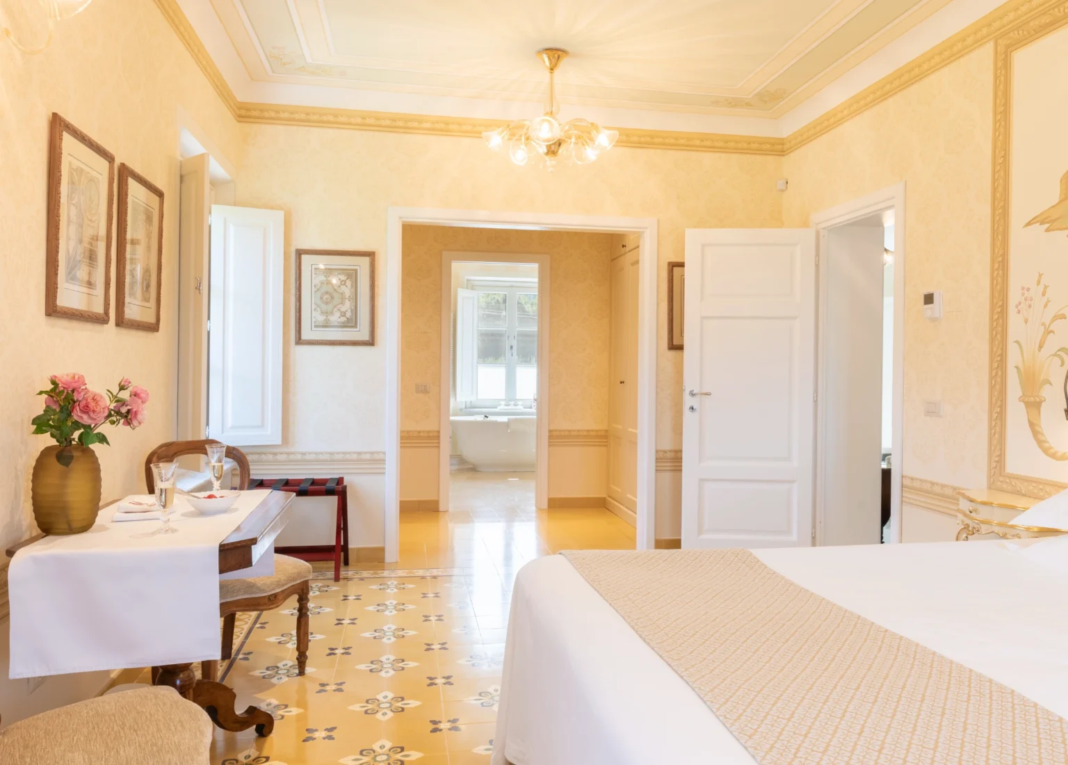 Luxurious bedroom interior of a villa in Italy, featuring elegant decor, a comfortable bed, a small dining table with flowers, and natural light illuminating the space. Ideal for vacation rentals in Italy. | Only on SopranoVillas