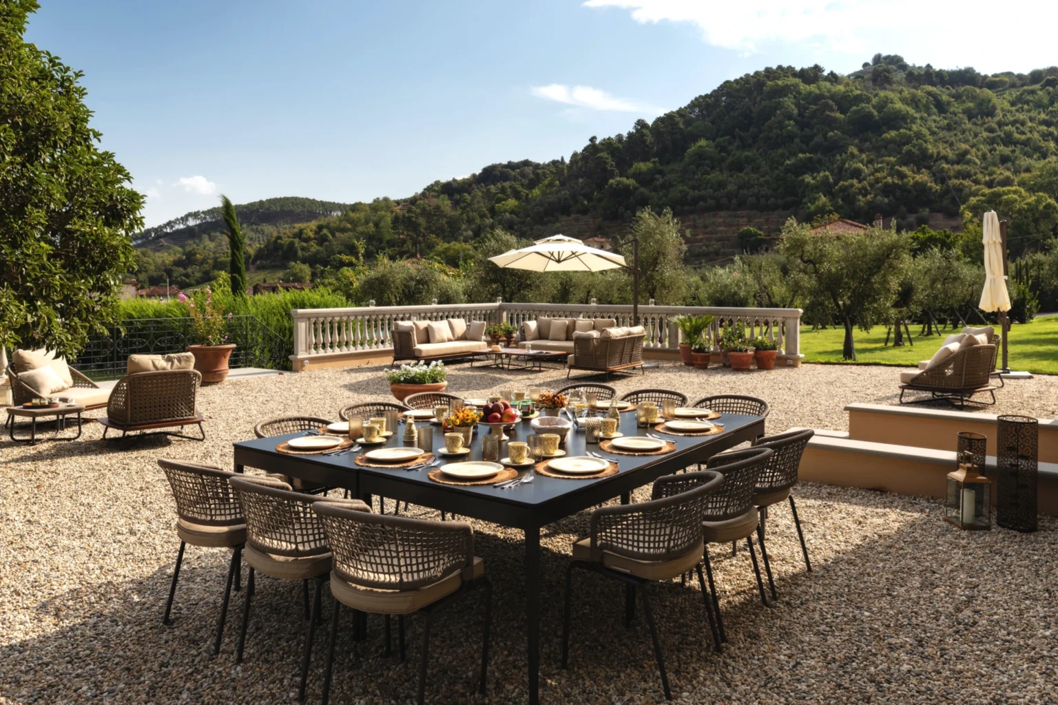 Luxury villa terrace in Italy featuring a spacious outdoor dining area, elegant table set for a meal, surrounded by lush greenery and scenic hills. Ideal for relaxing and entertaining in a picturesque setting. | Only on SopranoVillas