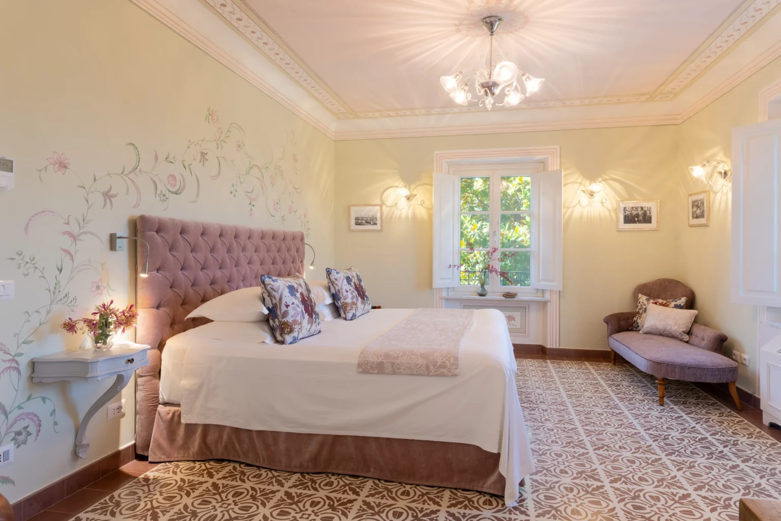 Luxurious bedroom in a villa for rent in Italy, featuring elegant decor, a plush bed with decorative pillows, and large windows that provide natural light and garden views. | Only on SopranoVillas