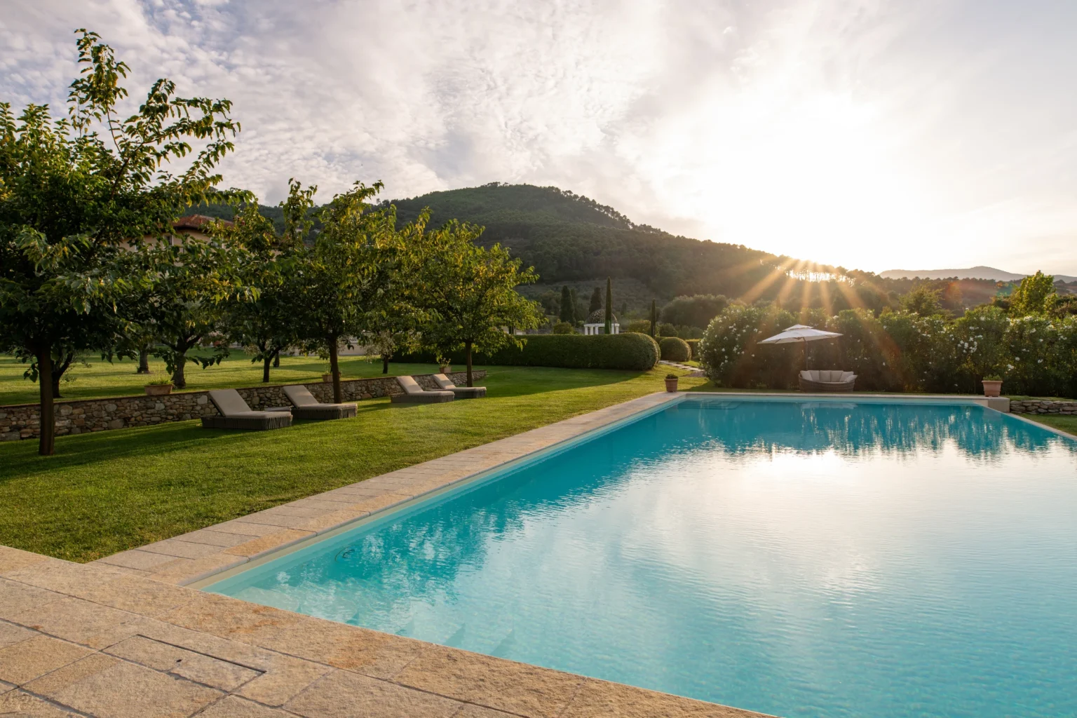 Luxury villa with a scenic pool and lush gardens in Italy, featuring stunning mountain views and a serene sunset. Perfect for vacation rentals. | Only on SopranoVillas