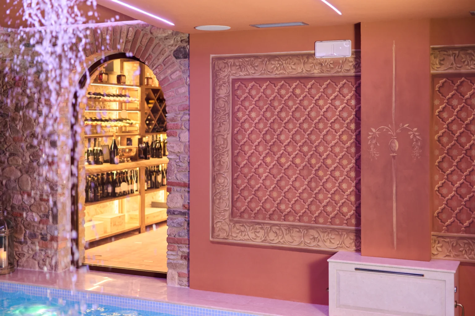 Luxurious indoor pool area of a villa in Italy, featuring elegant decor, a bar with a selection of fine wines, and a soothing water feature, ideal for relaxation and upscale living. | Only on SopranoVillas