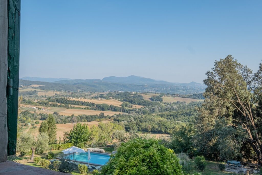 Scenic view of rolling hills and lush greenery with a swimming pool in the foreground, capturing the tranquil beauty of the countryside under a clear blue sky. | Only on SopranoVillas