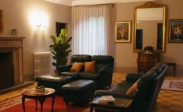 Cozy living room featuring dark leather sofas, a red area rug, and decorative artwork on the walls. Natural light filters through sheer curtains, highlighting a stylish coffee table and a potted plant, creating an inviting atmosphere.