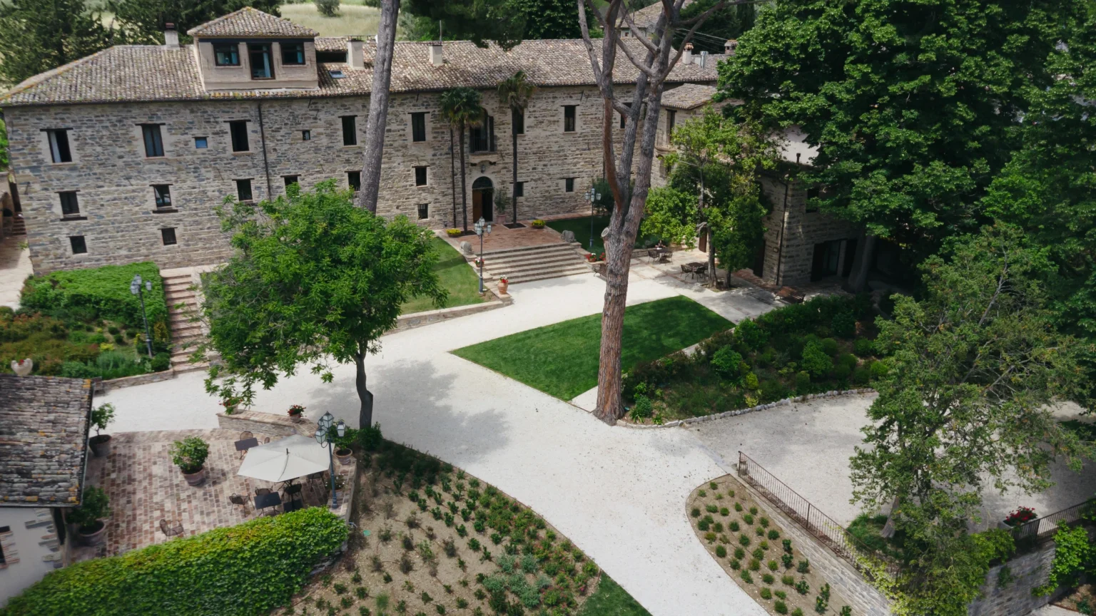 Aerial view of a charming stone villa surrounded by lush greenery, featuring a well-maintained garden, pathways, and outdoor seating areas. The villa's rustic architecture blends harmoniously with the natural landscape, creating a serene atmosphere ideal for relaxation and gatherings. | Only on SopranoVillas