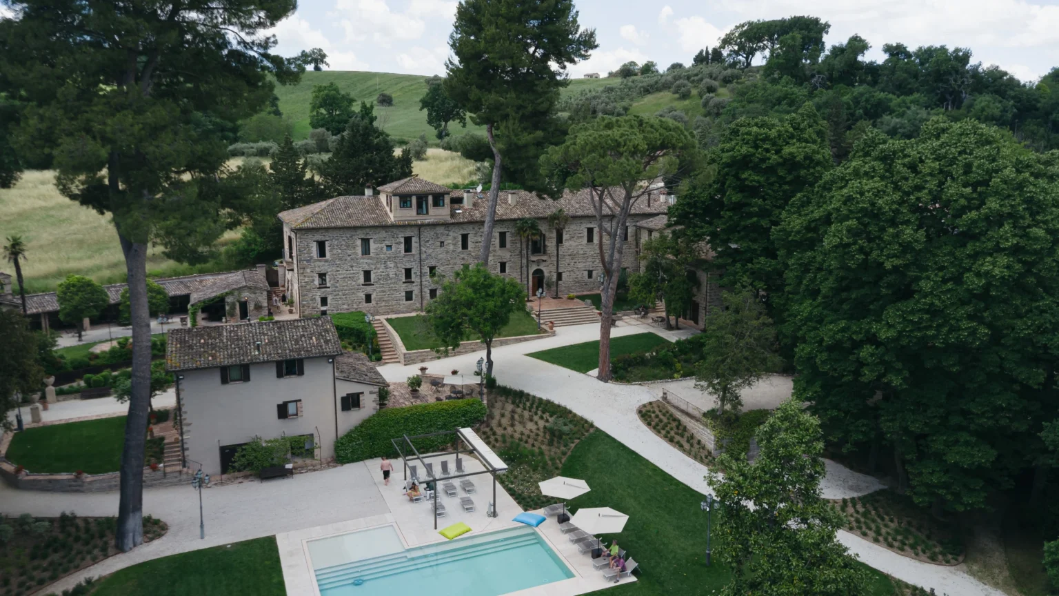 Aerial view of a luxurious stone villa surrounded by lush greenery, featuring a swimming pool and landscaped gardens, ideal for relaxation and outdoor activities. | Only on SopranoVillas