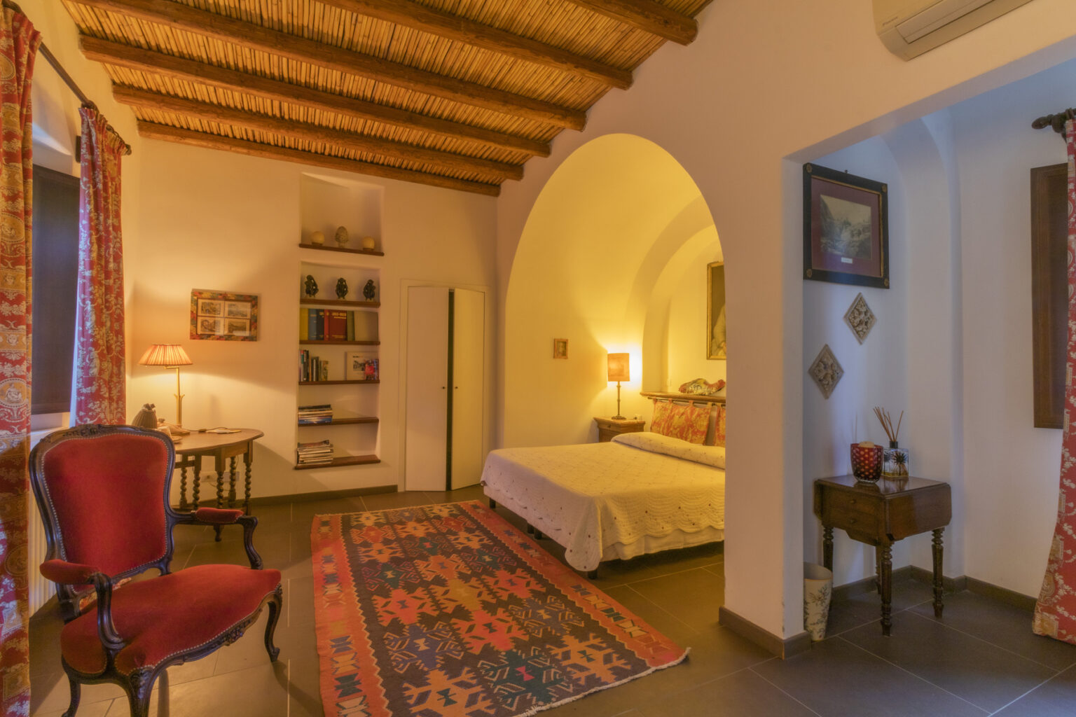 Cozy bedroom interior featuring a queen-sized bed, wooden ceiling beams, a vintage armchair, and decorative rugs, creating a warm and inviting atmosphere. | Only on SopranoVillas