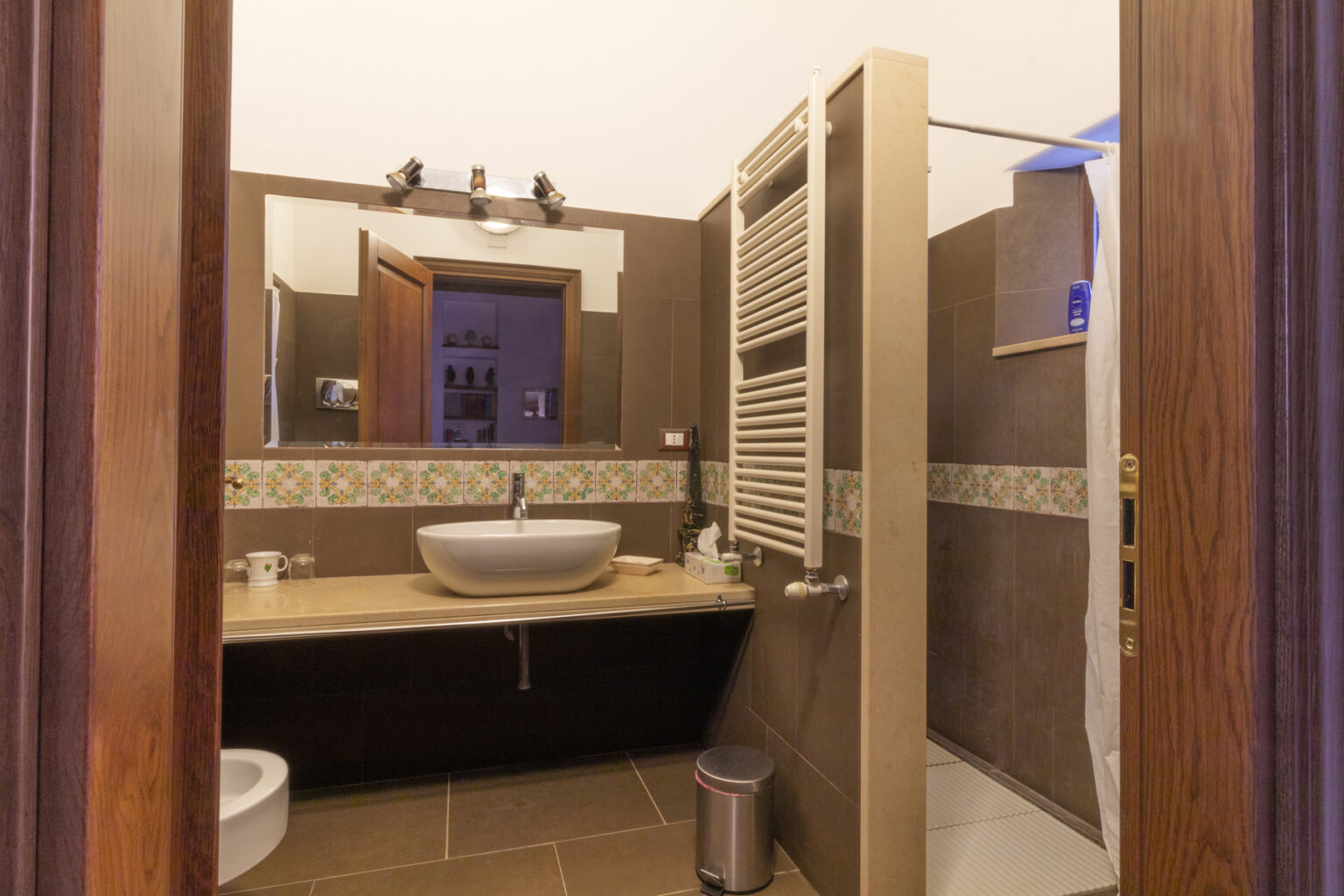 Modern bathroom interior featuring a stylish sink, wooden accents, and a spacious shower area, with warm lighting and elegant tile work. | Only on SopranoVillas
