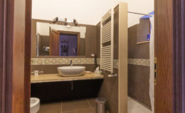 Modern bathroom interior featuring a stylish sink, wooden accents, and a spacious shower area, with warm lighting and elegant tile work.