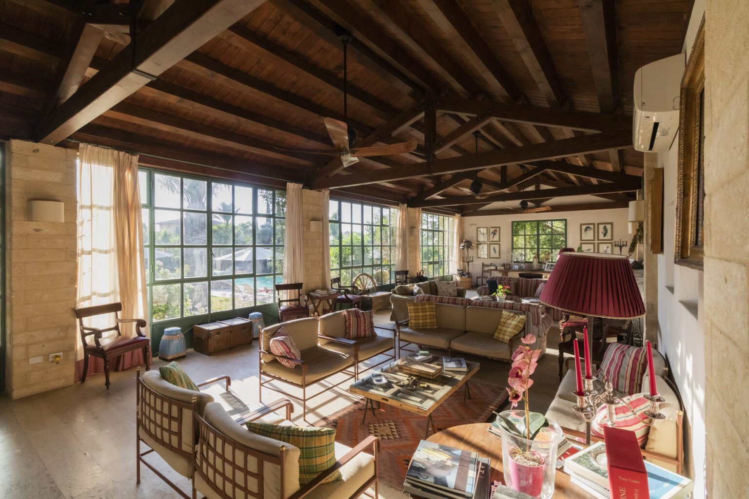Spacious and airy living room with wooden beams, large windows, and cozy seating arrangements, featuring colorful furniture and decorative elements for a warm, inviting atmosphere. | Only on SopranoVillas