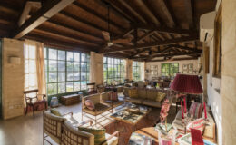 Spacious and airy living room with wooden beams, large windows, and cozy seating arrangements, featuring colorful furniture and decorative elements for a warm, inviting atmosphere.