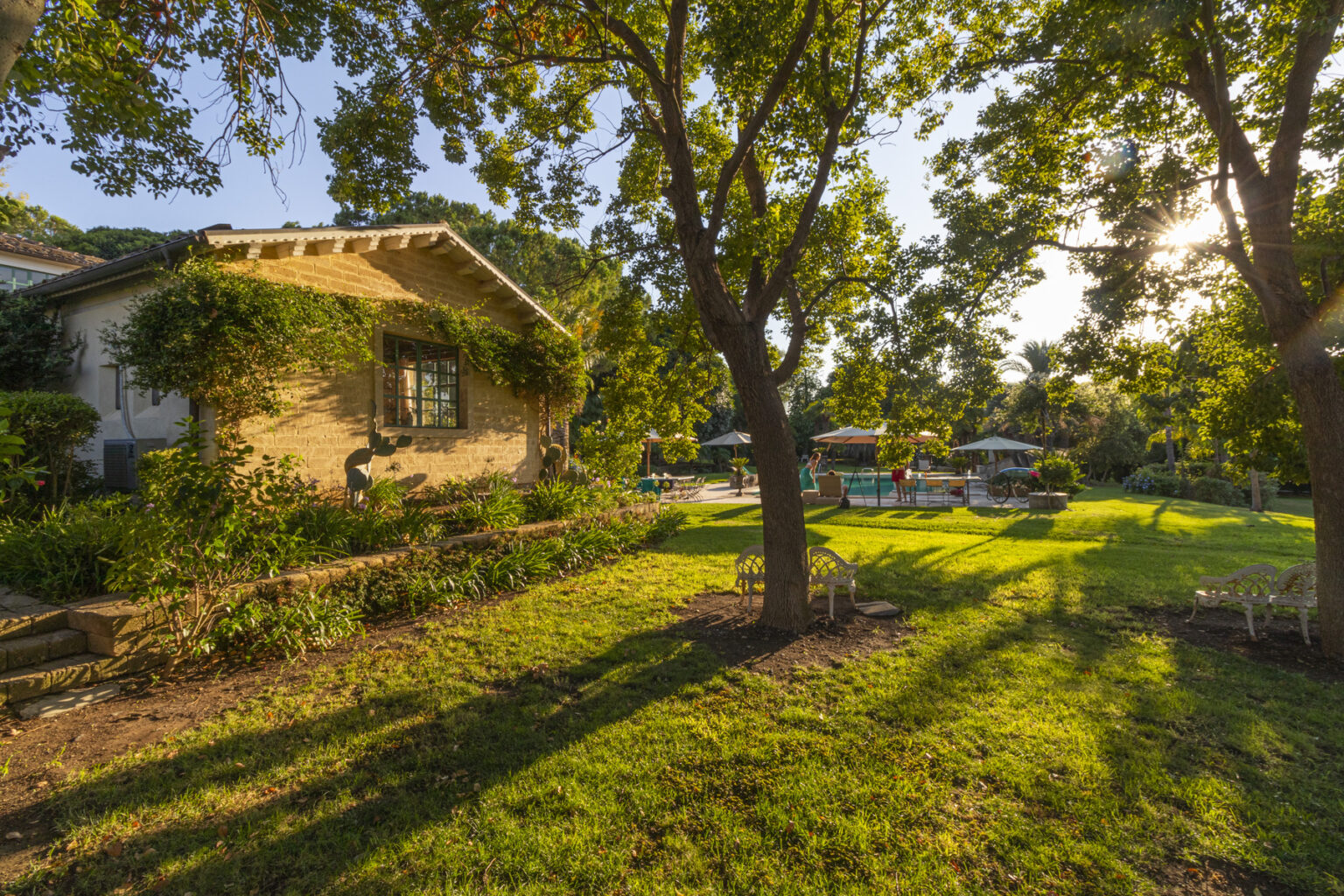 Charming rustic house surrounded by lush greenery, with a well-maintained garden and a serene outdoor pool area in the background, bathed in warm sunset light. | Only on SopranoVillas