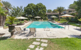 Luxurious backyard pool area featuring a sparkling blue pool, sun loungers, and shaded umbrellas surrounded by lush greenery and landscaped gardens. Perfect for relaxation and outdoor gatherings.
