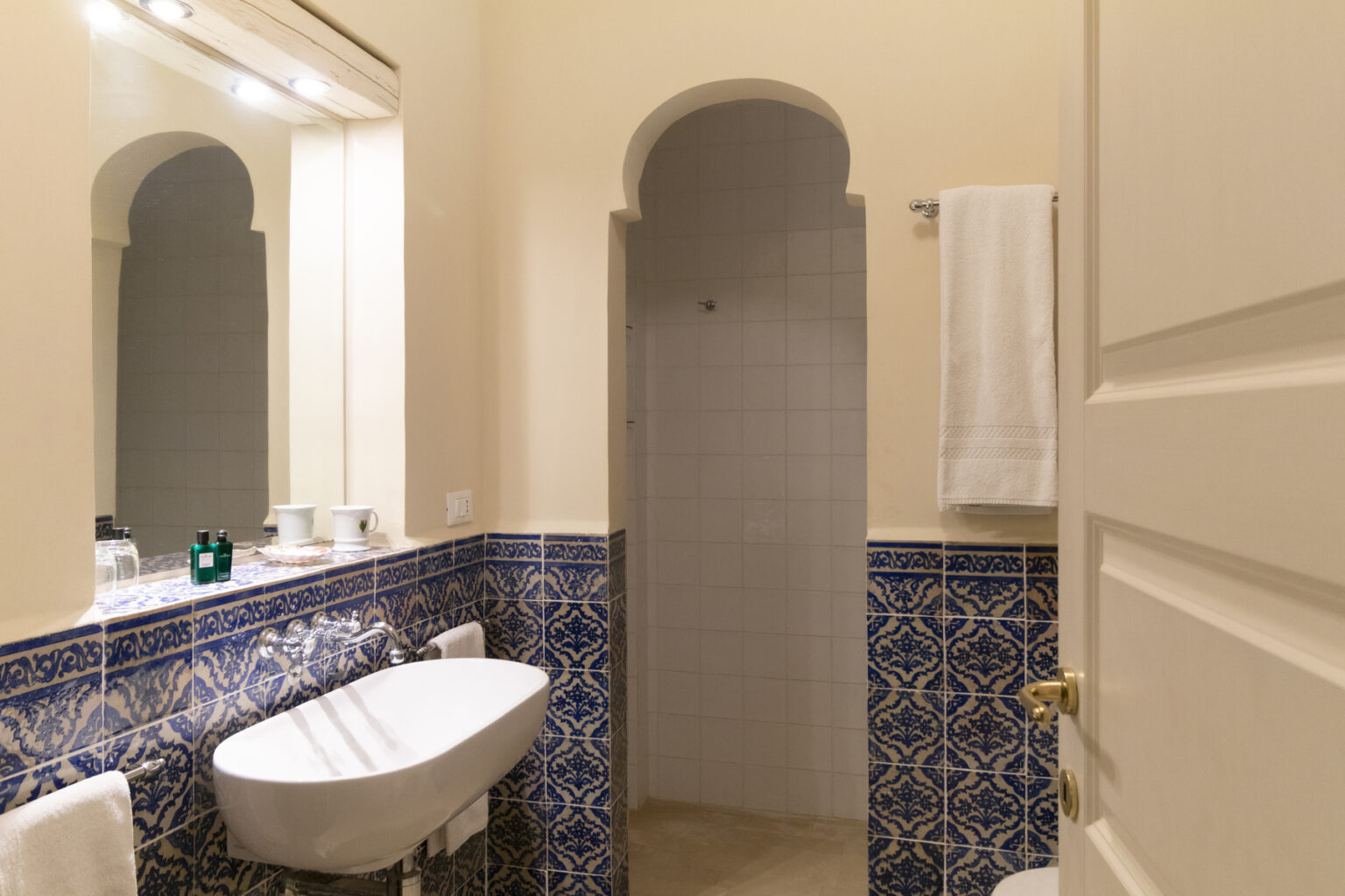 Modern bathroom interior featuring a bidet, shower, and decorative blue tile accents. The space includes a large mirror and a towel rack, providing a clean and stylish atmosphere. | Only on SopranoVillas