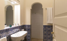 Modern bathroom interior featuring a bidet, shower, and decorative blue tile accents. The space includes a large mirror and a towel rack, providing a clean and stylish atmosphere.