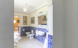Bright and spacious bathroom featuring blue tiled accents, a large mirror, modern fixtures, and decorative artwork on the walls, creating a welcoming atmosphere.