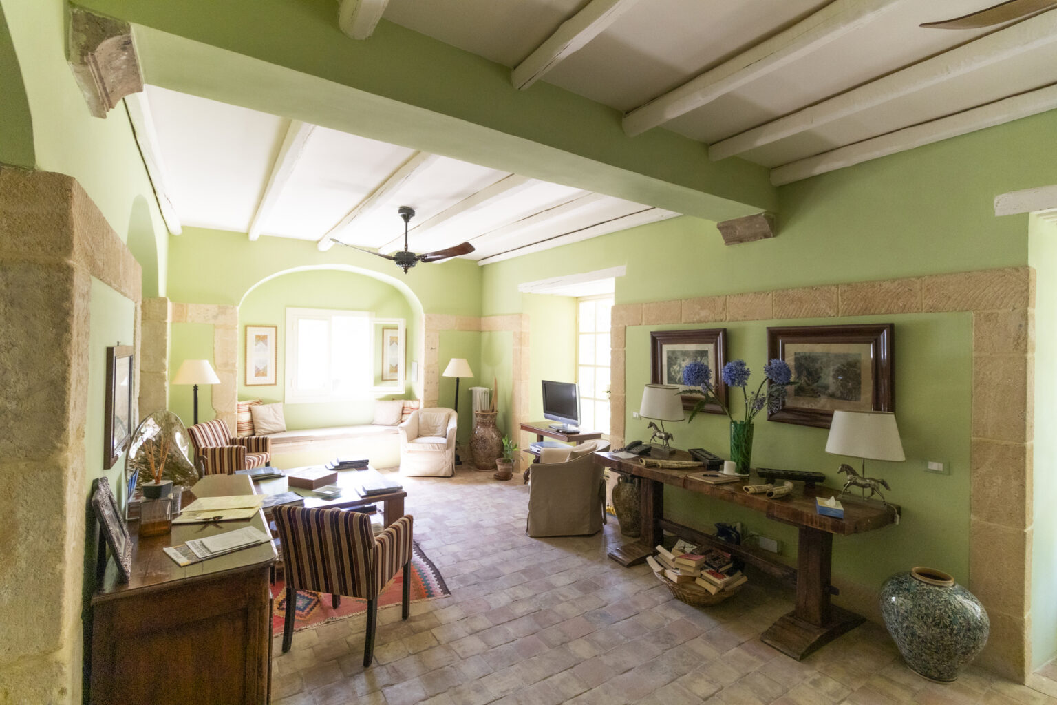 Spacious living room with green walls, wooden beams, and natural light, featuring comfortable seating, decorative artwork, and a cozy ambiance. | Only on SopranoVillas