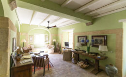 Spacious living room with green walls, wooden beams, and natural light, featuring comfortable seating, decorative artwork, and a cozy ambiance.