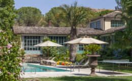 Luxurious villa with a swimming pool surrounded by lush greenery, featuring sun umbrellas and a stone fountain, ideal for relaxation and outdoor living.