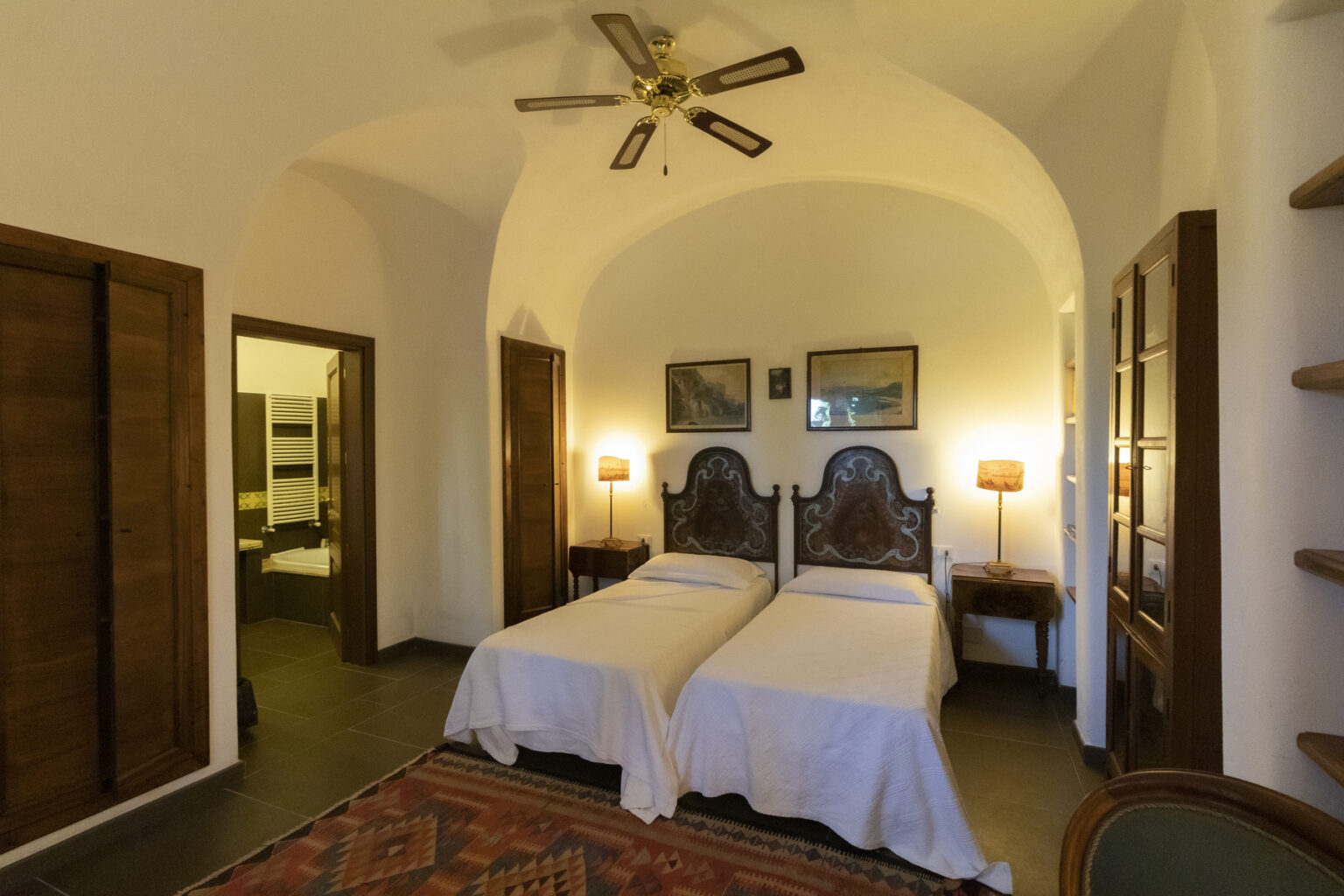 Cozy guest room featuring two twin beds, wooden furniture, and warm lighting, with arched ceilings and a decorative rug. Ideal for travelers seeking comfort and charm. | Only on SopranoVillas