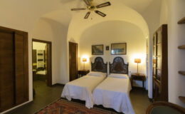 Cozy guest room featuring two twin beds, wooden furniture, and warm lighting, with arched ceilings and a decorative rug. Ideal for travelers seeking comfort and charm.