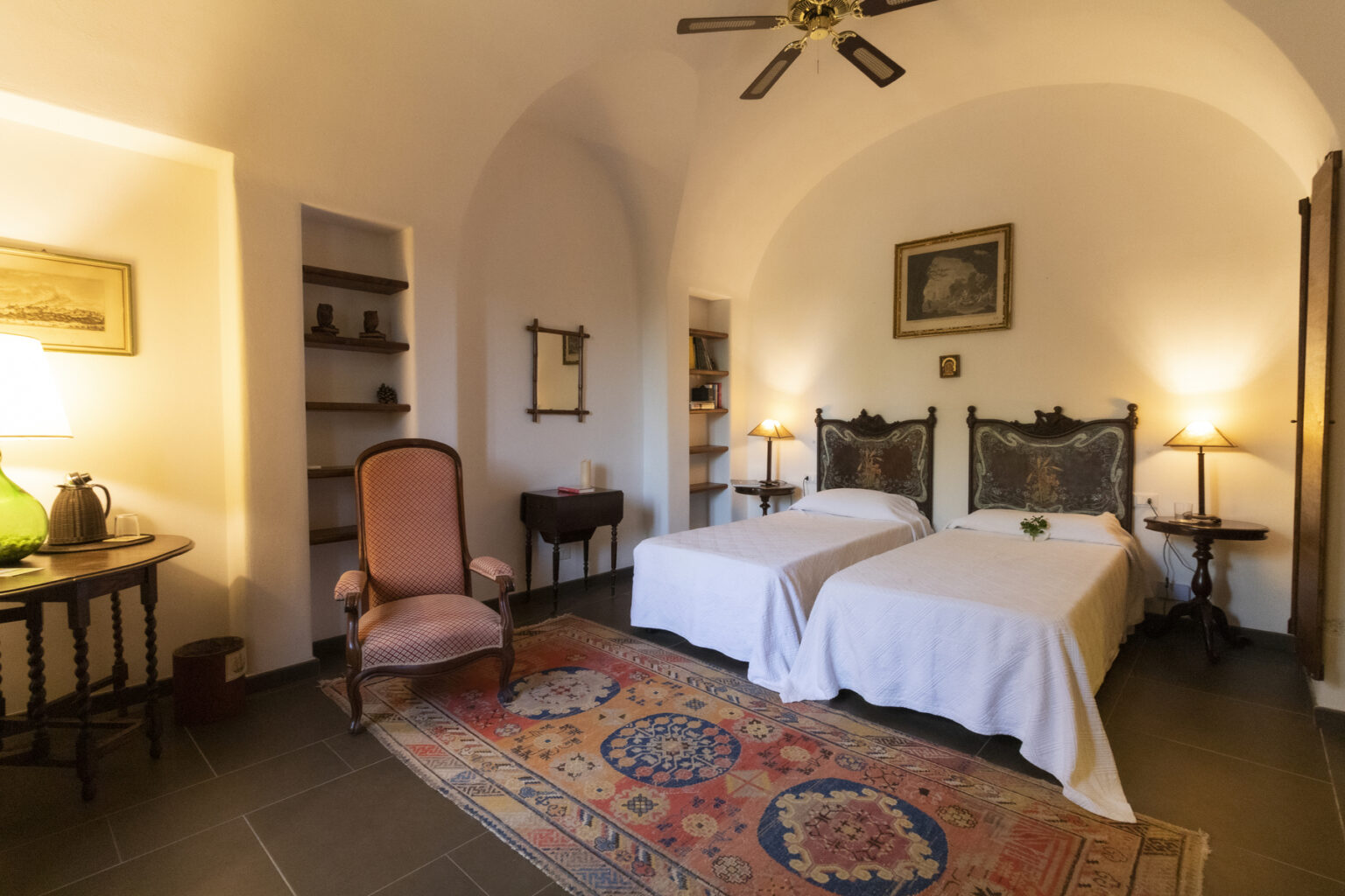 Cozy bedroom featuring two twin beds, a vintage armchair, and warm lighting, with an elegant rug and arched ceiling design. Ideal for relaxation and comfort. | Only on SopranoVillas