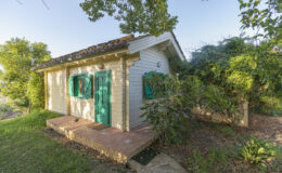 Charming small cottage with green shutters surrounded by lush greenery, offering a serene outdoor setting. Ideal for nature lovers and peaceful retreats.