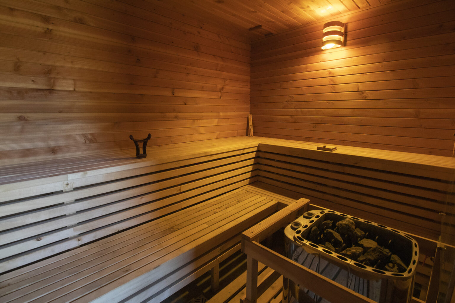 Interior of a wooden sauna featuring bench seating, a stone heater, and warm lighting, creating a relaxing atmosphere for wellness and rejuvenation. | Only on SopranoVillas