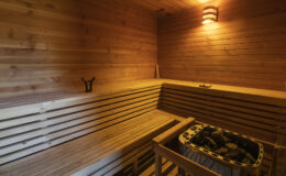 Interior of a wooden sauna featuring bench seating, a stone heater, and warm lighting, creating a relaxing atmosphere for wellness and rejuvenation.