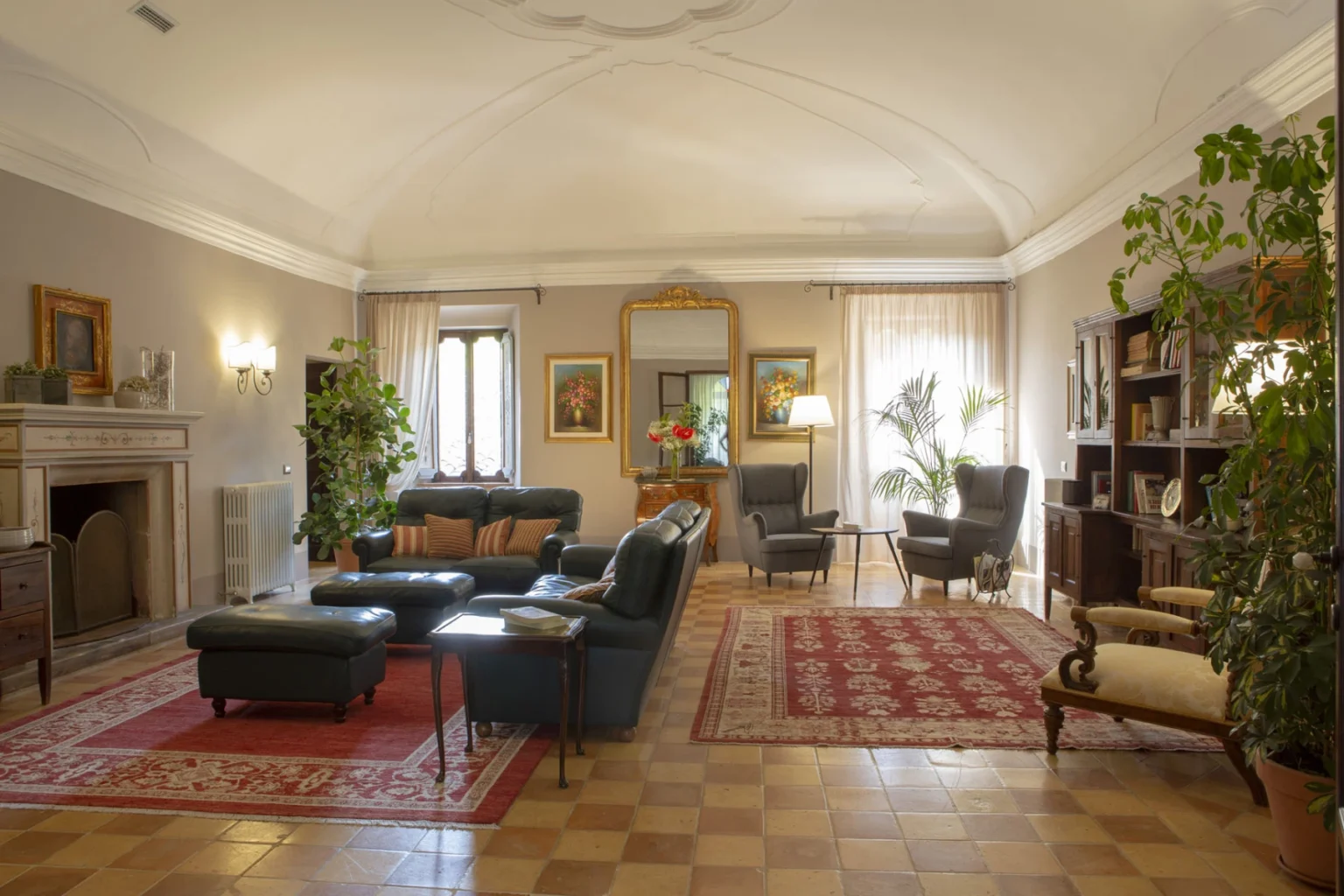 Spacious and elegantly designed living room featuring leather sofas, a decorative rug, and large windows with natural light. The room includes a fireplace, potted plants, and stylish artwork, creating a warm and inviting atmosphere. | Only on SopranoVillas