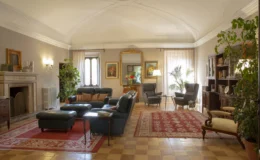 Spacious and elegantly designed living room featuring leather sofas, a decorative rug, and large windows with natural light. The room includes a fireplace, potted plants, and stylish artwork, creating a warm and inviting atmosphere.