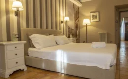 Cozy bedroom featuring a comfortable bed with white linens, decorative pillows, and stylish bedside lamps. The room has a warm color palette with striped wallpaper, a small nightstand, and elegant flooring. Ideal for relaxation and restful stays.