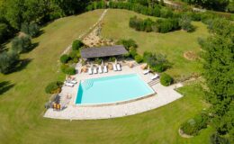 Aerial view of a luxurious swimming pool surrounded by a well-maintained garden, featuring lounge chairs and a shaded seating area, ideal for relaxation and outdoor gatherings in a serene landscape.