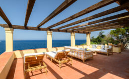 Stylish outdoor terrace with wooden beams and comfortable seating, overlooking a serene ocean view on a sunny day. Perfect for relaxation and entertaining.