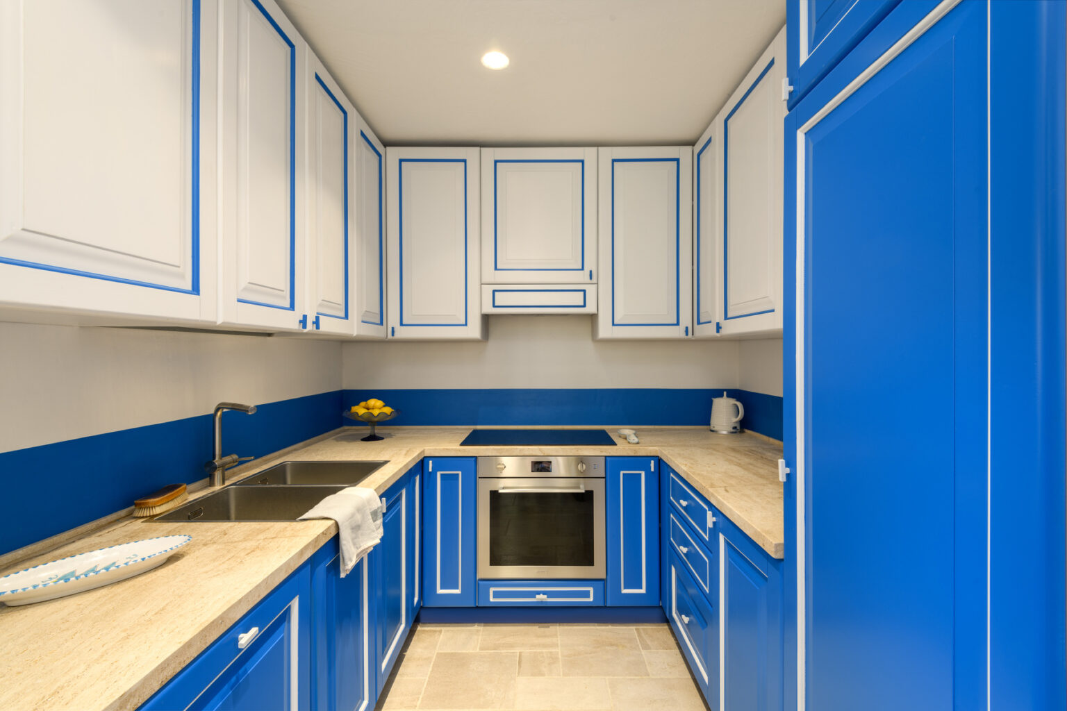 Modern kitchen with blue and white cabinetry, featuring a stainless steel oven, sink, and countertop. The design showcases a stylish blend of colors and efficient layout for cooking and dining. | Only on SopranoVillas