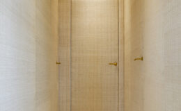 Interior view of a modern hallway featuring textured walls and two minimalist doors with gold handles, illuminated by soft lighting.