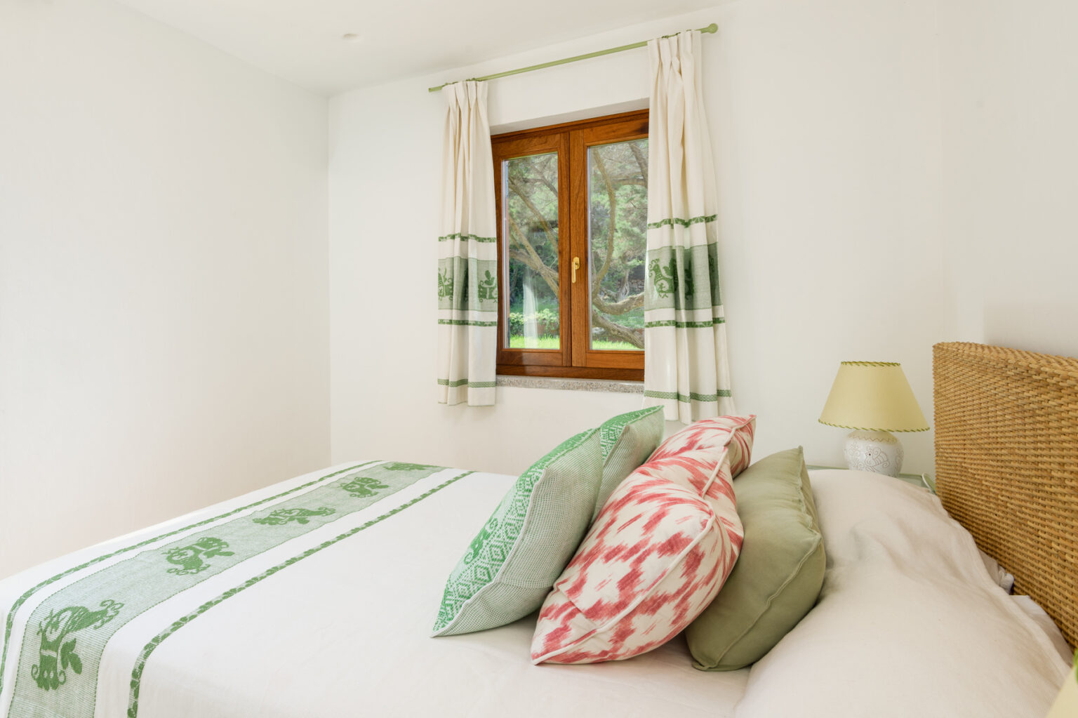 Bright and airy bedroom featuring a cozy bed with decorative pillows in green and pink hues, a wooden window with natural light, and light-colored curtains. Ideal for showcasing modern interior design and comfort. | Only on SopranoVillas
