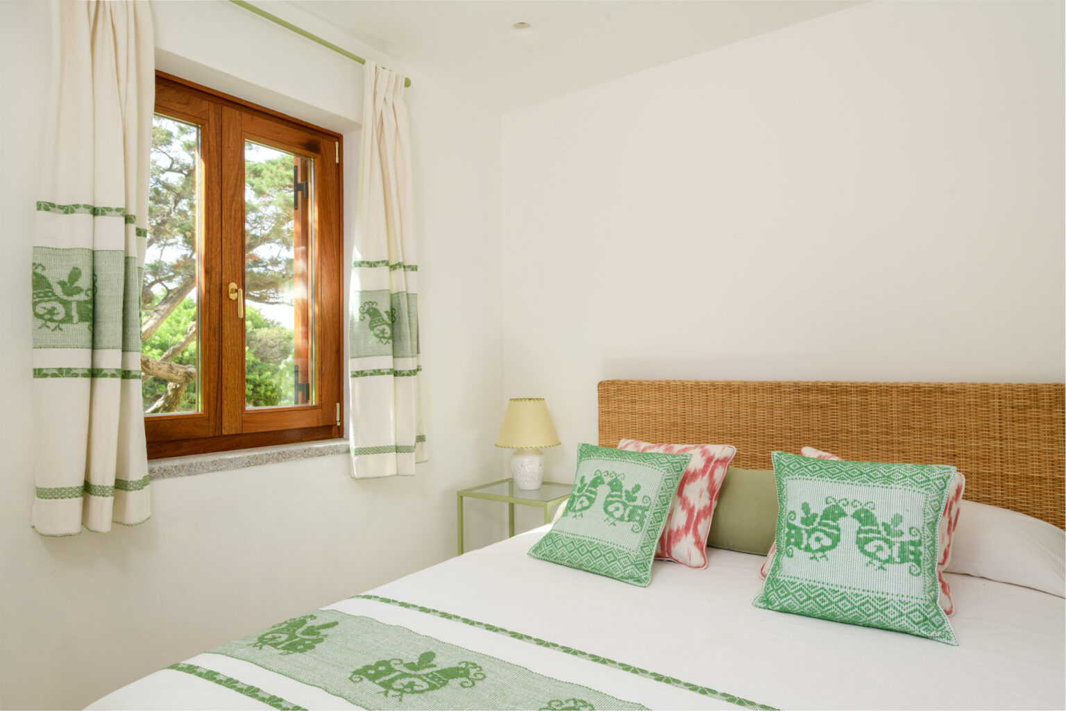 Cozy bedroom featuring a comfortable bed with green and pink decorative pillows, natural light streaming through a wooden window, and stylish curtains, creating a serene and inviting atmosphere. | Only on SopranoVillas