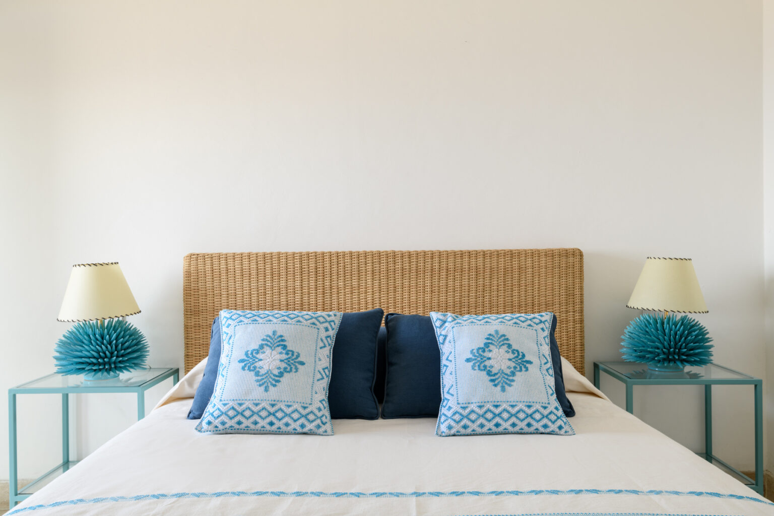 Modern bedroom interior featuring a woven headboard, blue and white decorative pillows, and stylish lamps on turquoise nightstands, creating a serene and inviting atmosphere. | Only on SopranoVillas