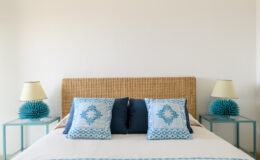 Modern bedroom interior featuring a woven headboard, blue and white decorative pillows, and stylish lamps on turquoise nightstands, creating a serene and inviting atmosphere.