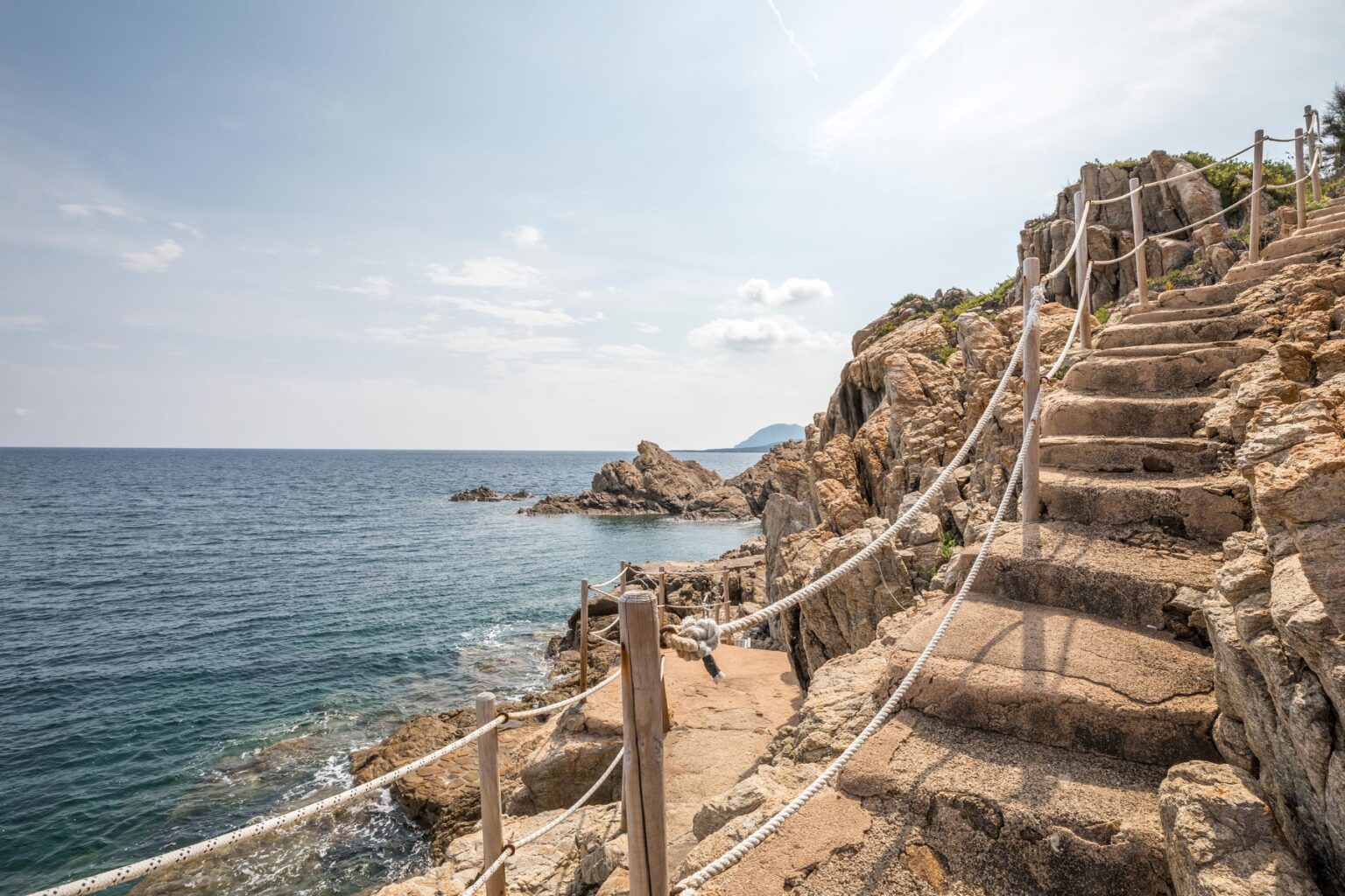 Stone steps leading down to a rocky coastline with a rope railing, surrounded by the ocean under a clear sky. Ideal for coastal hiking and scenic views. | Only on SopranoVillas