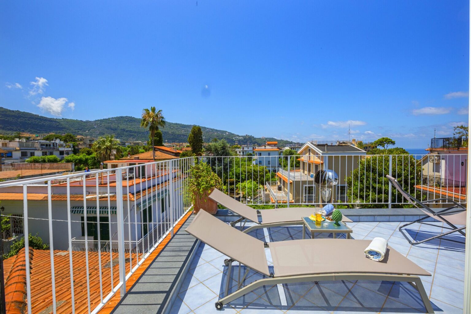 Rooftop terrace with sun loungers offering panoramic views of mountains and coastal houses under a clear blue sky, ideal for relaxation and outdoor living. | Only on SopranoVillas