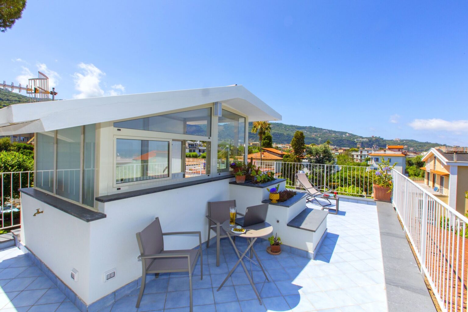 Modern rooftop terrace with seating area, panoramic views of surrounding hills and houses, and clear blue sky. Ideal for relaxation and outdoor dining. | Only on SopranoVillas
